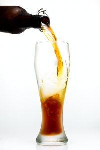 Dark beer is pouring from a bottle into a misted beer glass on a white background